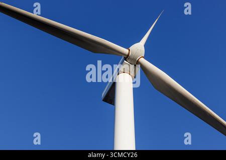 Vista ravvicinata di una moderna turbina eolica contro il cielo azzurro. Tecnologia delle energie rinnovabili e concetto di produzione sostenibile di energia elettrica. Foto Stock