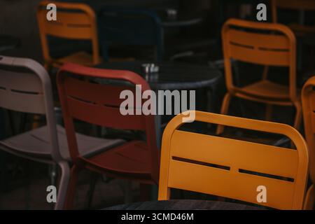 Colorate sedie gialle e rosse in un bar. Uno scatto ravvicinato di diverse sedie colorate disposte intorno ai tavoli, creando un'atmosfera vibrante e invitante. Foto Stock
