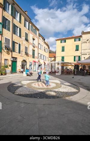 I bambini giocano accanto a ristoranti, caffetterie, annidati in stradine, strade e piazze. Nel centro storico di Finalborgo in Liguria, Italia. Foto Stock