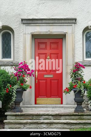 casa stuccata con porta d'ingresso rossa brillante e fiori in pentole Foto Stock