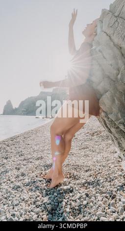Woman in a Dress si appoggia a Rock on a Pebble Beach Foto Stock