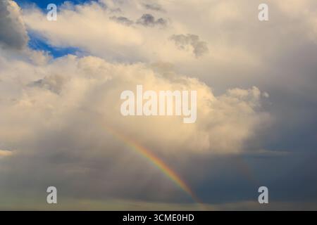 Un arcobaleno colorato appare tra le nuvole spettacolari dopo le piogge, con la luce del sole che attraversa e crea una tranquilla scena naturale del cielo. Foto Stock