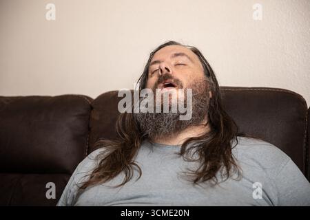 Un uomo con la barba e i capelli lunghi dorme su un divano Foto Stock