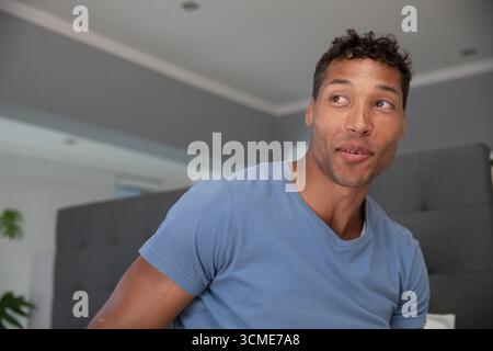 Uomo medio adulto che guarda direttamente nel soggiorno su un divano tufted grigio con plafoniere incassate Foto Stock