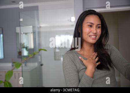 Donna asiatica in piedi, gestante in un bagno moderno con porta della doccia in vetro e lavandino, spazio copia Foto Stock