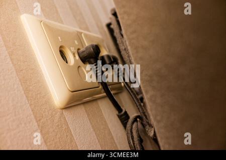Un pannello di presa bianco è posizionato su una parete a strisce. Due cavi per alimentazione e segnale antenna sono collegati a porte insolite. La scena semplice sembra tecnica Foto Stock