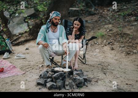 Coppia che si gode un falò in un ambiente boschivo durante un'escursione all'aperto rilassata Foto Stock