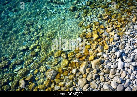 Acque turchesi del Mediterraneo ondulate con pietre rotonde che brillano alla luce del sole. Concetto di vacanza estiva Foto Stock