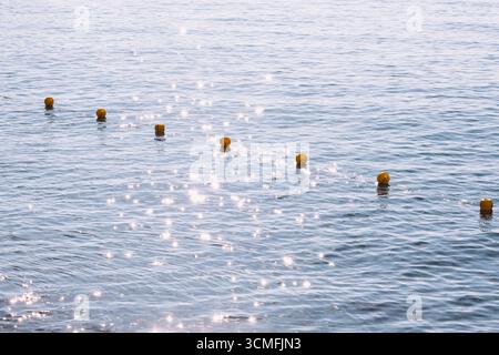 Il sole splende nella calma e ondeggiante acqua del Mar Mediterraneo con boe gialle. Concetto di vacanza estiva. Fotografia minimalista Foto Stock