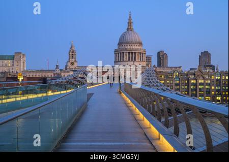 La folla passeggia lungo il Millennium Bridge mentre la cattedrale di St. Paul si illumina di sera. Foto Stock