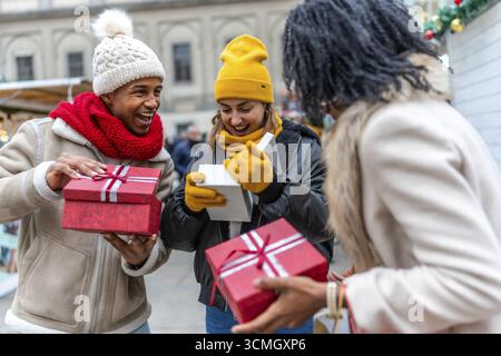 Felici amici multietnici che scambiano regali di natale in un mercatino di natale nel centro della città Foto Stock