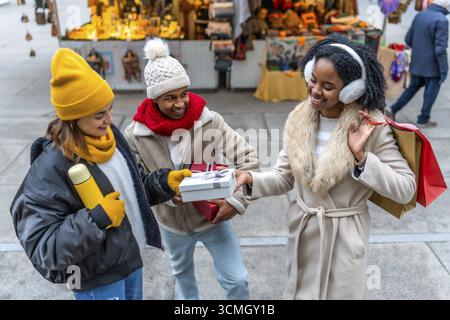 Felici amici multietnici che si scambiano regali di natale al mercatino di natale durante l'inverno Foto Stock