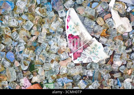Pezzi di ceramica rotta con un disegno floreale adagiati tra molti frammenti di vetro multicolore. Materiali riciclati per progetti artigianali fai da te Foto Stock
