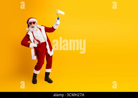 Babbo Natale si diverte in vacanza con un gesto creativo del rullo di pittura su un vibrante sfondo giallo in spirito festoso Foto Stock