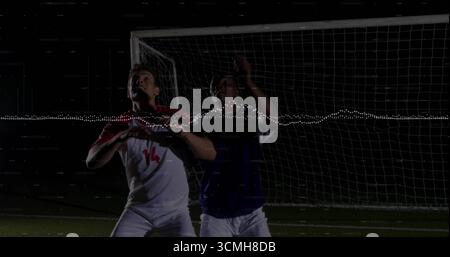 Giocatori di calcio che saltano indossando maglie palla da testa su prato illuminato, con effetto forma d'onda e rete porta Foto Stock