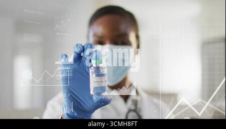 Tenendo in mano il ricercatore che indossa maschera e guanti analizzando i dati della cartella nel laboratorio ospedaliero, con la fiala COVID-19 Foto Stock
