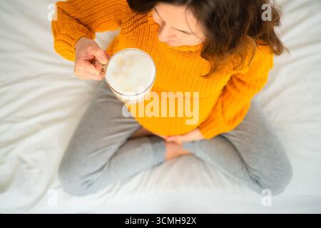 Primo piano aereo di donne incinte che si godono il latte in posa meditativa, riflettendo sulle linee guida alimentari. Calda atmosfera di piacere consapevole. Foto Stock