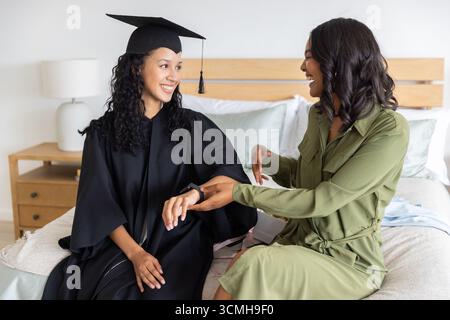Mamma e figlia adolescente diverse che celebrano la laurea indossando abito e mensa a letto Foto Stock