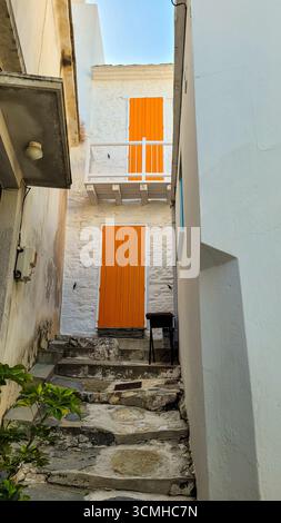 Un affascinante vicolo stretto con gradini di pietra e una porta arancione luminosa nella tradizionale Chora di Skopelos, Grecia Foto Stock