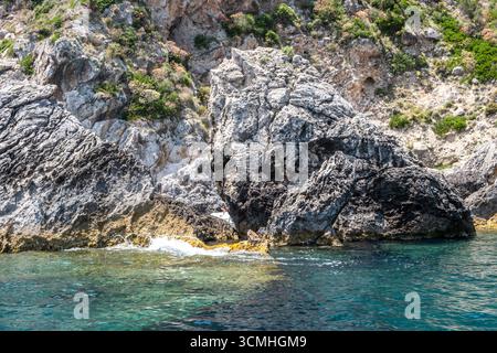 Le ripide scogliere rocciose sorgono dal mare turchese, dai riflessi della luce del sole sull'acqua ondulata, dall'isola di Corfù in Grecia e da Paleokastritsa Foto Stock