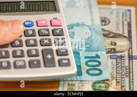 Real brasiliano e denaro in dollari. Banconote brasiliane e statunitensi e una calcolatrice tascabile portatile. Concetto finanziario, cambio valuta, tasso di mercato, bambola Foto Stock
