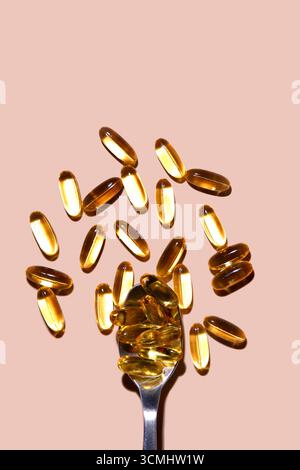 Più capsule di olio di pesce sono sparse su uno sfondo rosa, con un cucchiaio che ne raccoglie alcune Foto Stock