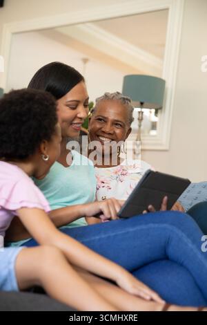 Diverse famiglie sedute sul divano in soggiorno interagiscono mentre utilizzano il tablet insieme Foto Stock