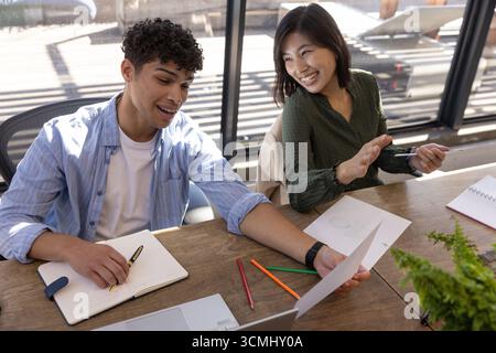 Colleghi diversi che collaborano al tavolo nello spazio di coworking, rivedendo gli appunti con tablet e notebook Foto Stock