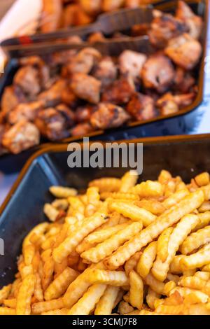 Sfrigolante banchetto di cibo di strada: Salsicce alla griglia, shashlik e patatine fritte dorate in contenitori da asporto in un ristorante all'aperto. Foto Stock