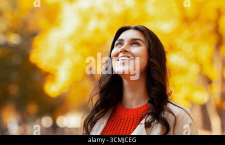 Ritratto di splendida giovane donna in autunno vestito sorridente e. guardando a piedi al parco Foto Stock
