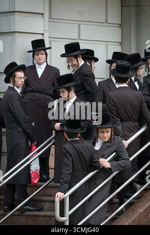 Gli studenti della yeshivah, vestiti allo stesso modo, si riuniscono in attesa di un autobus da portare a una sessione di preghiera stagionale. A New York. Foto Stock