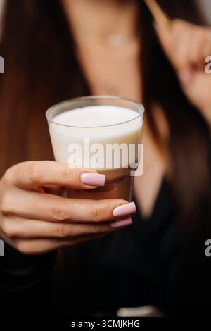 Dessert a strati con crema di latte e cioccolato in un bicchiere, tenuto dalle donne Foto Stock