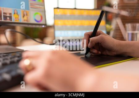 Primo piano delle mani che lavorano con la penna stilo e il pad da disegno, migliorando il contenuto delle foto sul monitor del desktop e sul laptop. Flusso di lavoro di editing produttivo con dispositivi digitali in creative home studio. Foto Stock