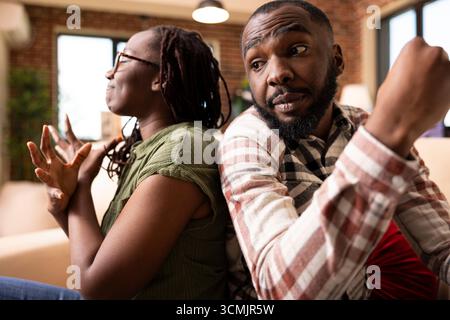 Coppia nera che affronta un conflitto di relazioni a casa. La donna afroamericana sembra scoraggiata con gli occhi chiusi mentre il fidanzato parla con gesti espressivi durante una conversazione difficile. Foto Stock
