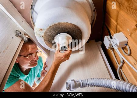 L'idraulico installa il tubo di ingresso del sifone sotto il lavello della cucina lavorando in spazi ristretti. Foto Stock