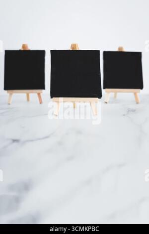 tre tele nere su cavalletti miniaturizzati su scrivania in marmo bianco, sfondo mockup minimalista per aggiungere testo o design, dof poco profondo Foto Stock