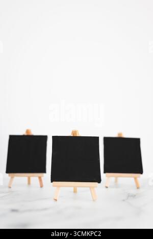tre tele nere su cavalletti miniaturizzati su scrivania in marmo bianco, sfondo mockup minimalista per aggiungere testo o design, dof poco profondo Foto Stock