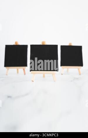 tre tele nere su cavalletti miniaturizzati su scrivania in marmo bianco, sfondo mockup minimalista per aggiungere testo o design, dof poco profondo Foto Stock