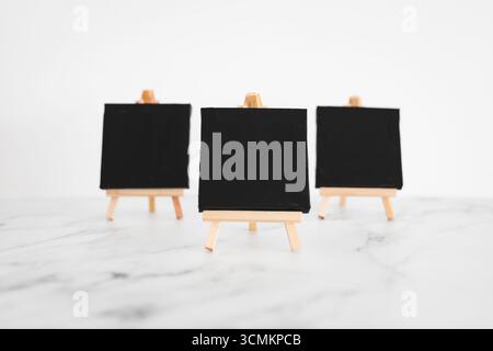 tre tele nere su cavalletti miniaturizzati su scrivania in marmo bianco, sfondo mockup minimalista per aggiungere testo o design, dof poco profondo Foto Stock