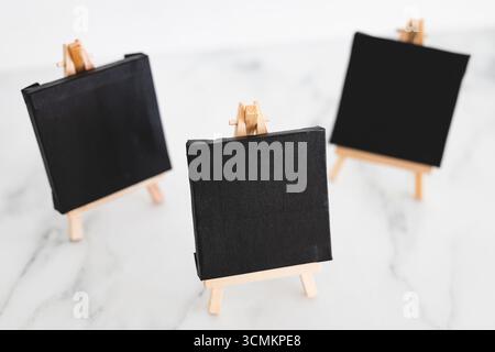tre tele nere su cavalletti miniaturizzati su scrivania in marmo bianco, sfondo mockup minimalista per aggiungere testo o design, dof poco profondo Foto Stock