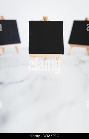 tre tele nere su cavalletti miniaturizzati su scrivania in marmo bianco, sfondo mockup minimalista per aggiungere testo o design, dof poco profondo Foto Stock