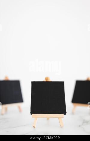 tre tele nere su cavalletti miniaturizzati su scrivania in marmo bianco, sfondo mockup minimalista per aggiungere testo o design, dof poco profondo Foto Stock