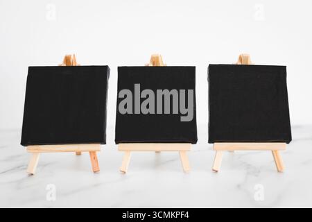 tre tele nere su cavalletti miniaturizzati su scrivania in marmo bianco, sfondo mockup minimalista per aggiungere testo o design, dof poco profondo Foto Stock