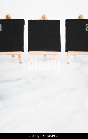 tre tele nere su cavalletti miniaturizzati su scrivania in marmo bianco, sfondo mockup minimalista per aggiungere testo o design, dof poco profondo Foto Stock