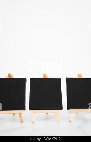 tre tele nere su cavalletti miniaturizzati su scrivania in marmo bianco, sfondo mockup minimalista per aggiungere testo o design, dof poco profondo Foto Stock