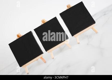 tre tele nere su cavalletti miniaturizzati su scrivania in marmo bianco, sfondo mockup minimalista per aggiungere testo o design, dof poco profondo Foto Stock