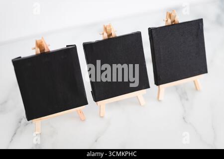 tre tele nere su cavalletti miniaturizzati su scrivania in marmo bianco, sfondo mockup minimalista per aggiungere testo o design, dof poco profondo Foto Stock