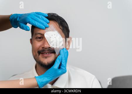 Sorridente uomo di mezza età che riceve un cerotto protettivo per gli occhi da un operatore sanitario che indossa guanti dopo l'intervento chirurgico, concetto di trattamento medico, lesioni recov Foto Stock