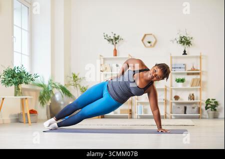Donna afroamericana Plus size che si allunga durante l'allenamento domestico Foto Stock