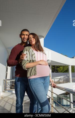 Diverse coppie in piedi sul balcone sotto le colonne che tengono ringhiere metalliche e appoggiano la mano sulla pancia Foto Stock